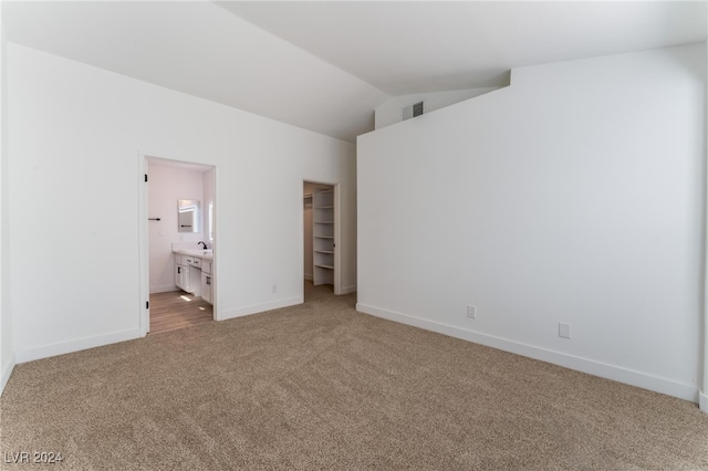 unfurnished bedroom with vaulted ceiling, a spacious closet, a closet, carpet flooring, and ensuite bath