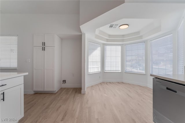 kitchen featuring white cabinetry, light hardwood / wood-style floors, a raised ceiling, and stainless steel dishwasher