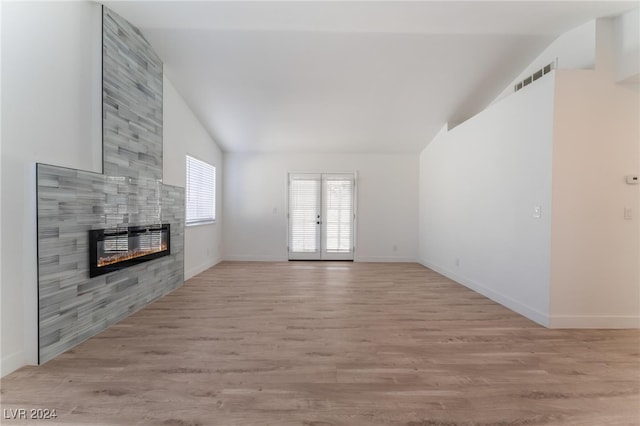 unfurnished living room featuring french doors, light wood-type flooring, a tiled fireplace, and vaulted ceiling