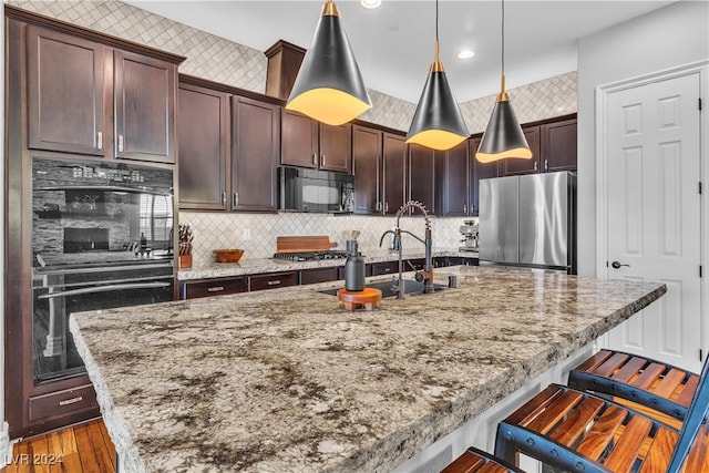 kitchen with backsplash, a breakfast bar, wood-type flooring, black appliances, and decorative light fixtures