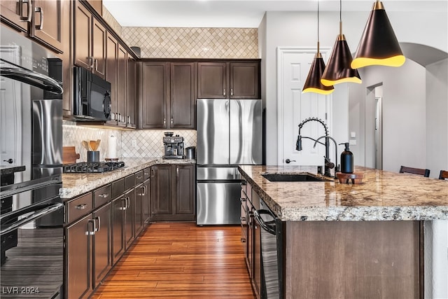 kitchen featuring hardwood / wood-style flooring, an island with sink, hanging light fixtures, stainless steel appliances, and sink