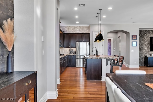 kitchen with appliances with stainless steel finishes, dark hardwood / wood-style flooring, dark brown cabinetry, pendant lighting, and a kitchen island with sink