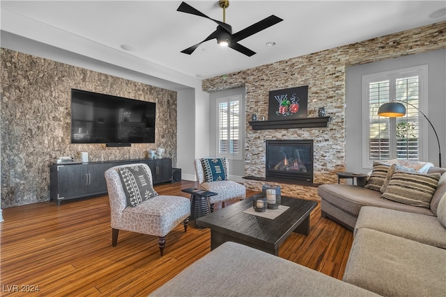 living room featuring ceiling fan, a stone fireplace, and dark hardwood / wood-style flooring