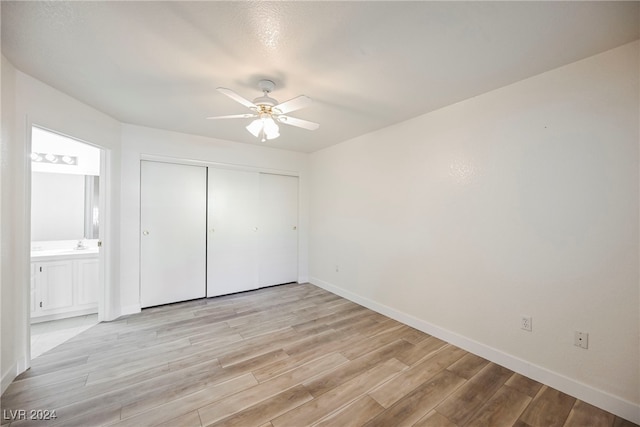 unfurnished bedroom with a closet, ensuite bath, light wood-type flooring, and ceiling fan