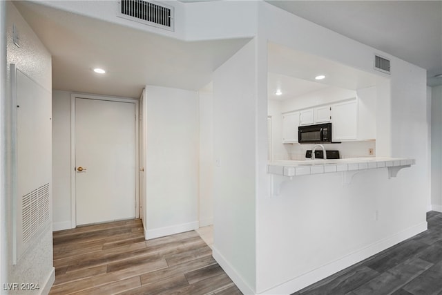 kitchen featuring tile countertops, dark hardwood / wood-style flooring, kitchen peninsula, a kitchen breakfast bar, and white cabinetry