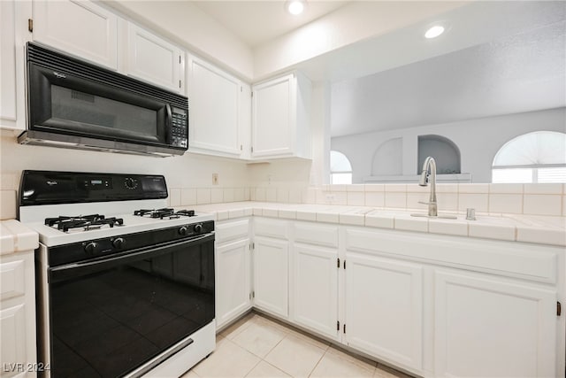 kitchen with white cabinets, white gas range, light tile patterned floors, tile countertops, and sink