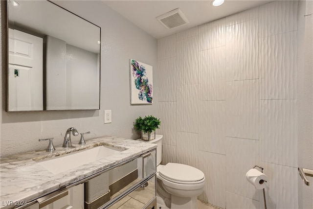 bathroom featuring tile patterned flooring, vanity, toilet, and tile walls