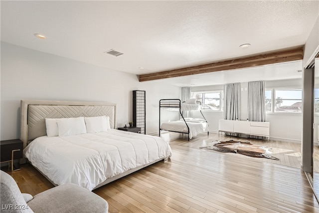 bedroom with beamed ceiling, wood-type flooring, and a textured ceiling