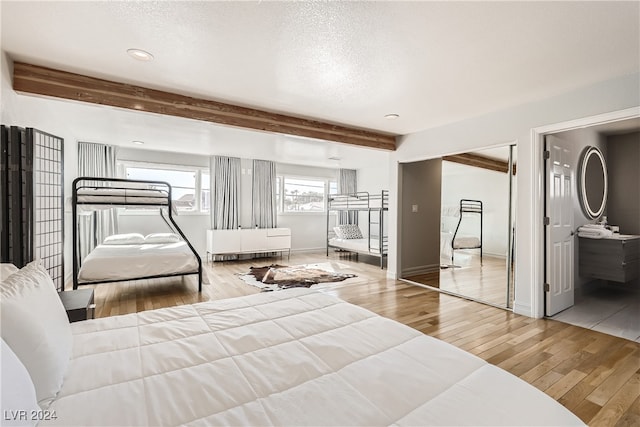 bedroom with a textured ceiling, light hardwood / wood-style floors, beam ceiling, and a closet