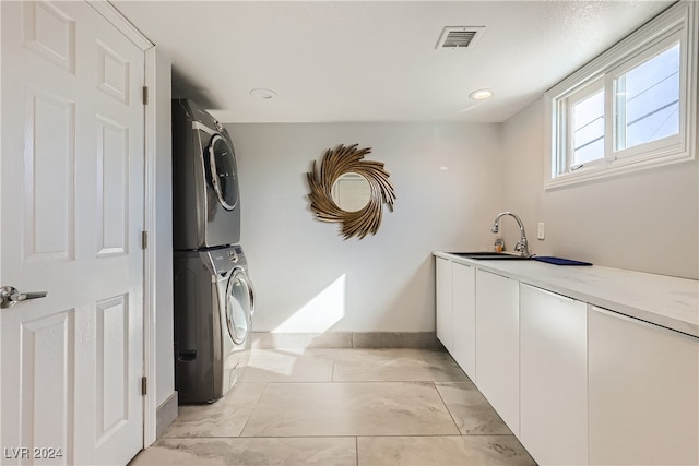 clothes washing area featuring cabinets, stacked washer and dryer, and sink