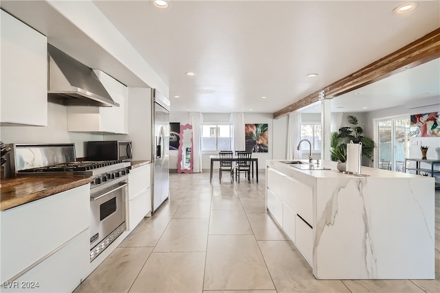 kitchen featuring appliances with stainless steel finishes, wall chimney exhaust hood, a kitchen island with sink, sink, and white cabinets