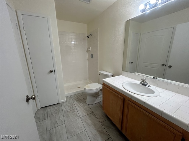 bathroom featuring tiled shower, vanity, and toilet