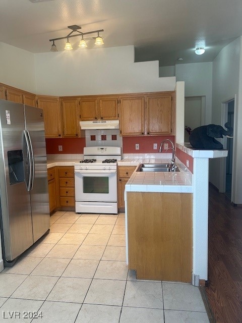 kitchen with gas range gas stove, sink, kitchen peninsula, stainless steel fridge with ice dispenser, and tile counters