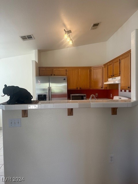 kitchen featuring kitchen peninsula, stainless steel appliances, a kitchen breakfast bar, tile counters, and vaulted ceiling