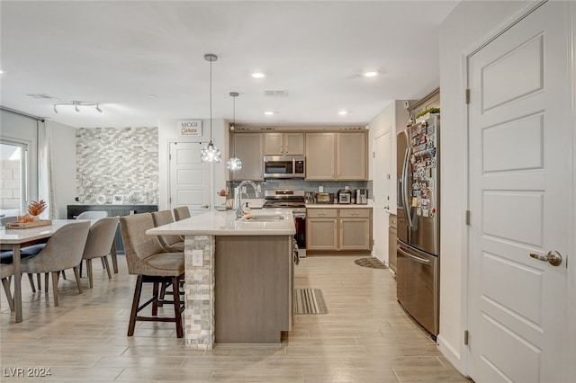 kitchen with backsplash, a center island with sink, light brown cabinets, appliances with stainless steel finishes, and decorative light fixtures