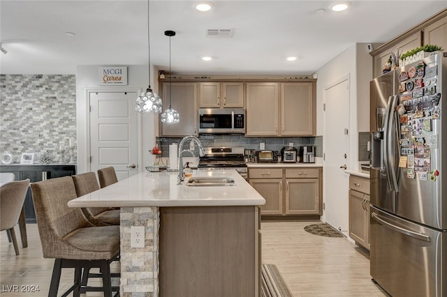 kitchen with sink, tasteful backsplash, decorative light fixtures, appliances with stainless steel finishes, and light wood-type flooring