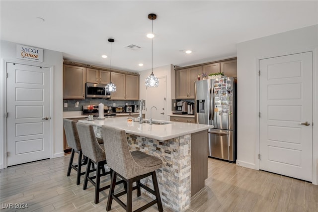 kitchen featuring pendant lighting, sink, a kitchen island with sink, light hardwood / wood-style flooring, and stainless steel appliances