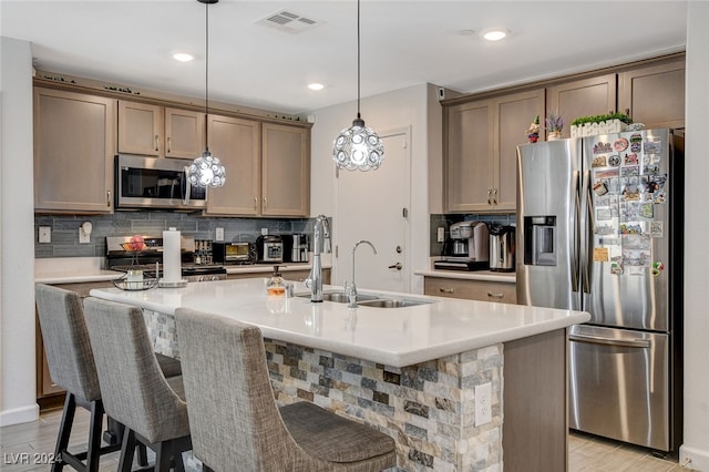 kitchen featuring light hardwood / wood-style floors, decorative light fixtures, a kitchen island with sink, appliances with stainless steel finishes, and a kitchen bar