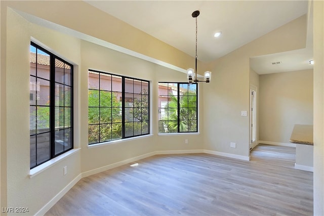 unfurnished dining area with vaulted ceiling, a chandelier, and light wood-type flooring