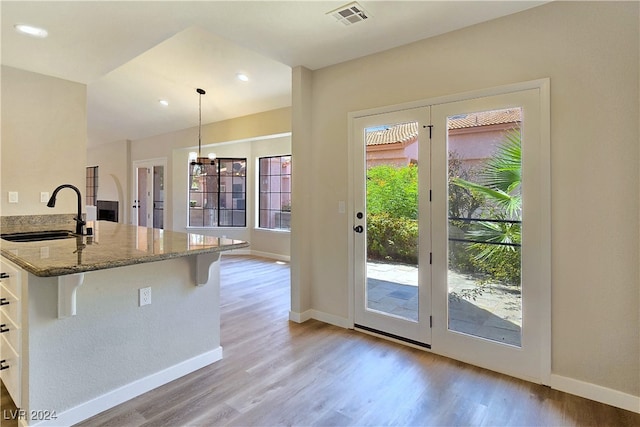 kitchen featuring hanging light fixtures, light stone countertops, sink, and light wood-type flooring