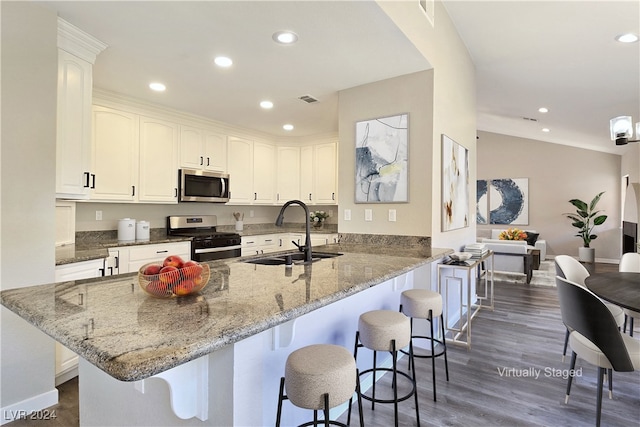 kitchen with sink, a breakfast bar, white cabinetry, gas range, and kitchen peninsula