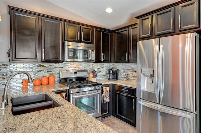 kitchen with lofted ceiling, stainless steel appliances, sink, light stone counters, and tasteful backsplash