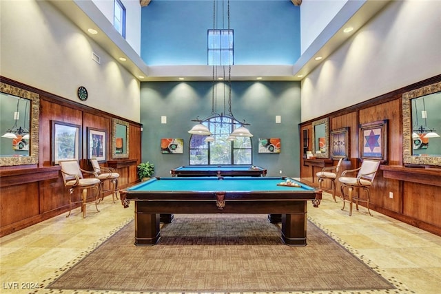 recreation room featuring wood walls, a high ceiling, and plenty of natural light