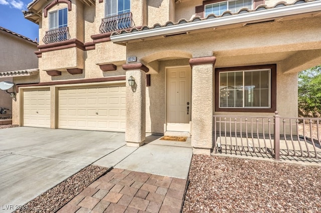 entrance to property with concrete driveway, a tiled roof, an attached garage, and stucco siding