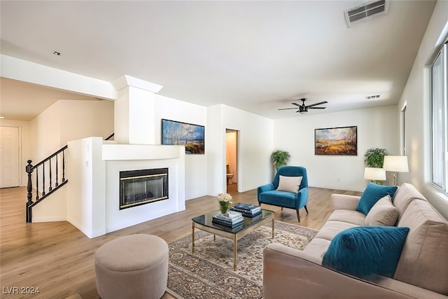 living room featuring light wood-type flooring, visible vents, a glass covered fireplace, and stairs