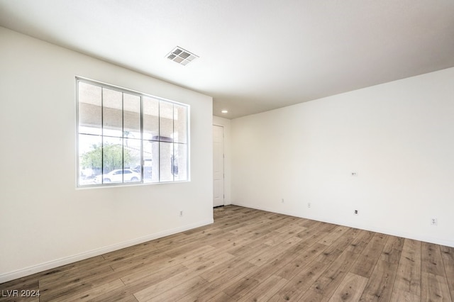 spare room with light wood-type flooring, visible vents, and baseboards