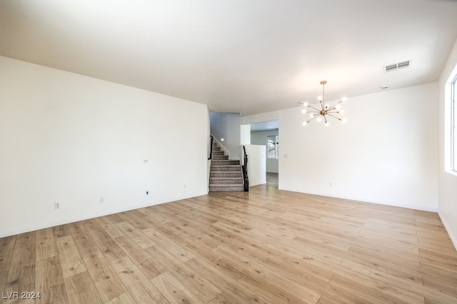 empty room featuring stairway, light wood-type flooring, visible vents, and an inviting chandelier