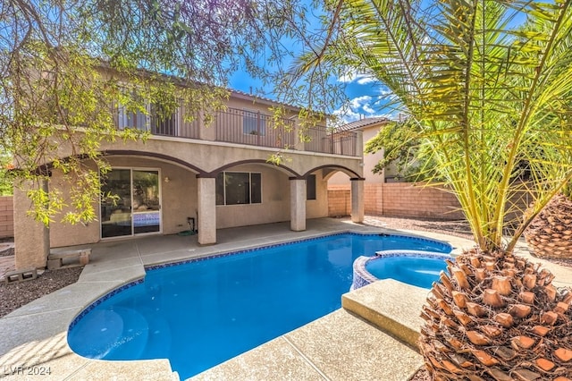 rear view of property featuring a balcony, a pool with connected hot tub, a patio, and stucco siding