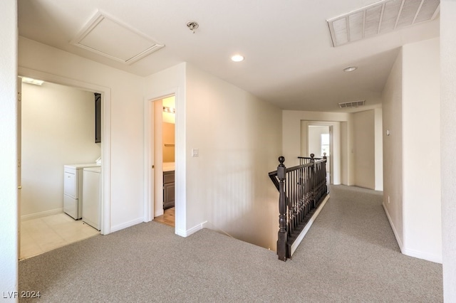 corridor featuring attic access, visible vents, washer and clothes dryer, light colored carpet, and an upstairs landing