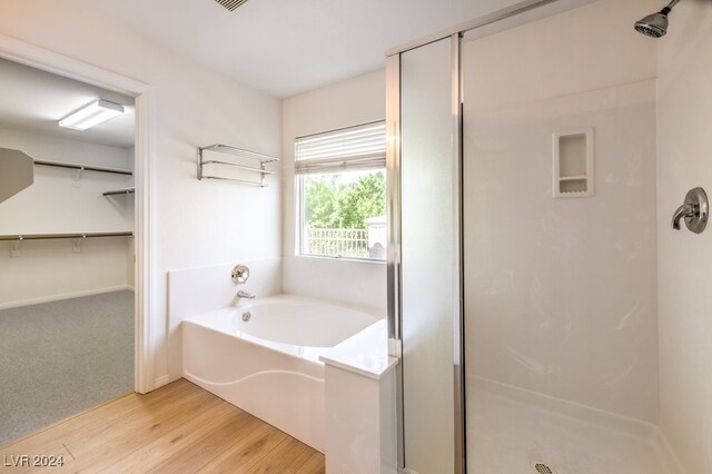 bathroom featuring wood finished floors, a shower stall, a bath, and a walk in closet