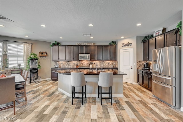 kitchen with a kitchen breakfast bar, a kitchen island with sink, stainless steel appliances, and light wood-type flooring