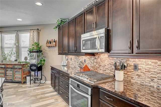 kitchen featuring appliances with stainless steel finishes, dark brown cabinetry, light hardwood / wood-style floors, and dark stone countertops