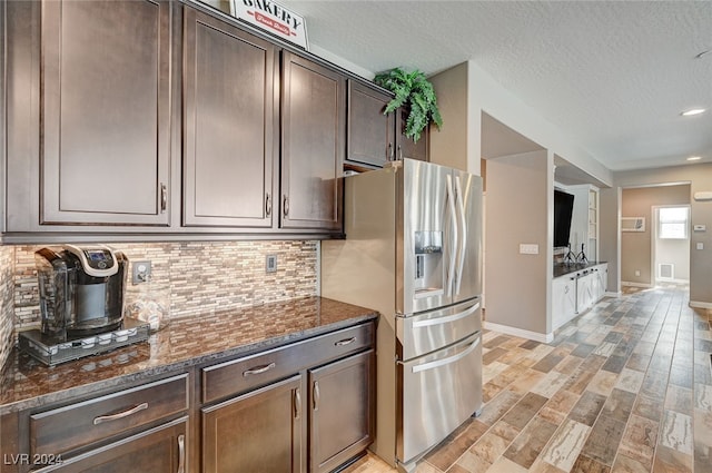 kitchen featuring decorative backsplash, dark brown cabinetry, a textured ceiling, dark stone countertops, and stainless steel fridge with ice dispenser