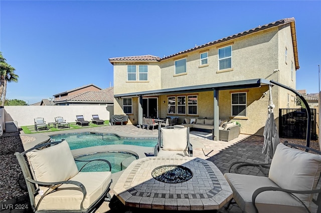 rear view of property featuring a swimming pool with hot tub, a patio area, and an outdoor living space with a fire pit