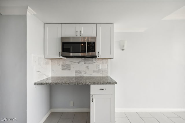 kitchen featuring stone counters, built in desk, white cabinetry, decorative backsplash, and light tile patterned floors