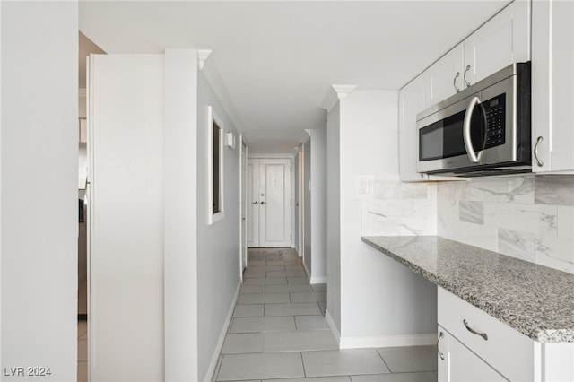 kitchen featuring light stone countertops, decorative backsplash, white cabinets, and light tile patterned floors