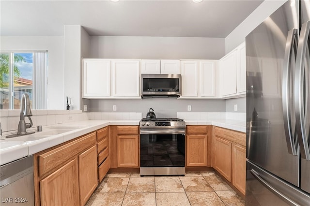 kitchen with sink, white cabinetry, appliances with stainless steel finishes, tile counters, and light tile patterned floors