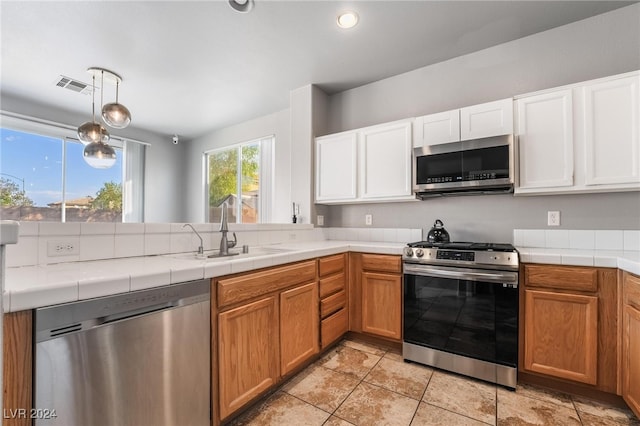 kitchen with white cabinets, pendant lighting, light tile patterned floors, sink, and stainless steel appliances