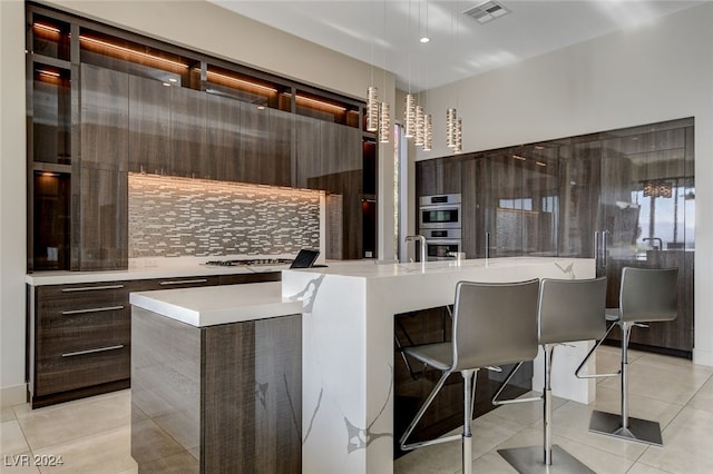 kitchen with double oven, light tile patterned flooring, a center island with sink, and a breakfast bar