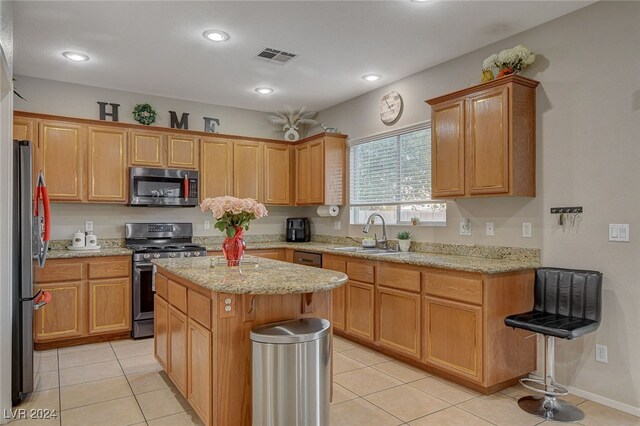 kitchen featuring sink, light tile patterned floors, a kitchen island, appliances with stainless steel finishes, and light stone countertops