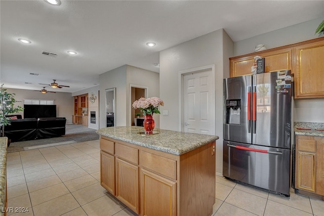 kitchen featuring light stone countertops, ceiling fan, a center island, stainless steel fridge, and light tile patterned floors