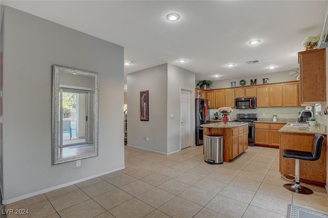 kitchen with light tile patterned flooring, a kitchen island, light stone counters, sink, and stainless steel appliances