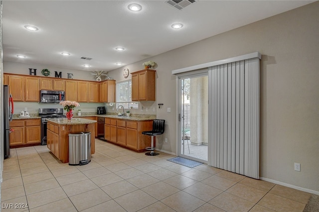 kitchen with light tile patterned flooring, sink, stainless steel appliances, light stone countertops, and a center island