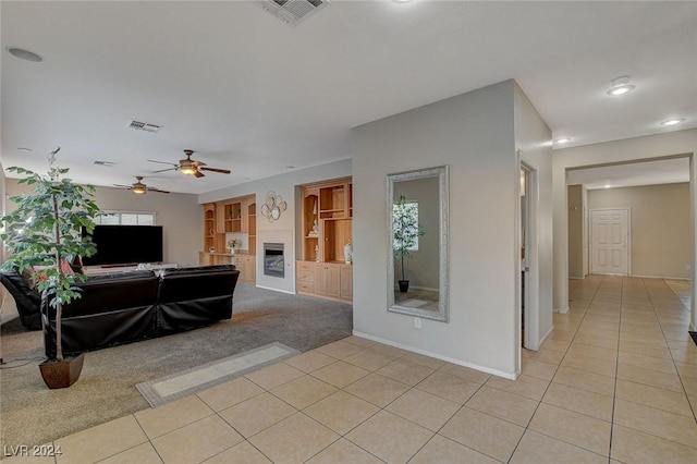 living room featuring light tile patterned floors, a fireplace, visible vents, ceiling fan, and light carpet