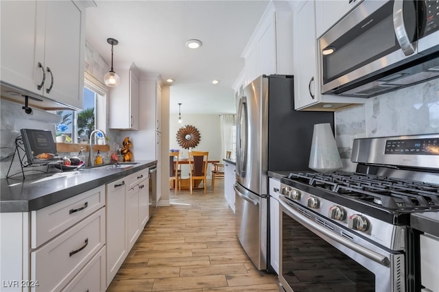 kitchen with white cabinets, sink, decorative light fixtures, light hardwood / wood-style flooring, and appliances with stainless steel finishes