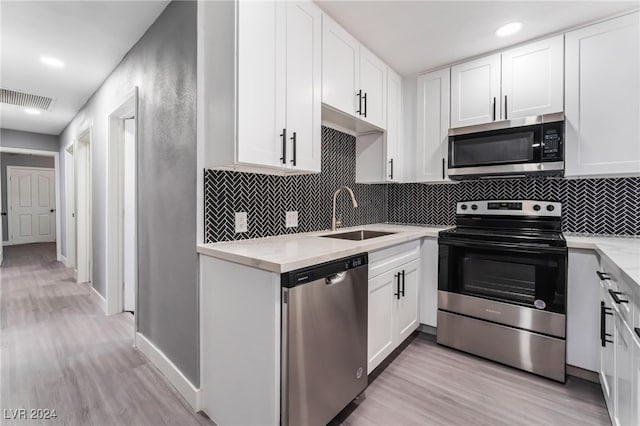 kitchen with white cabinets, sink, light hardwood / wood-style flooring, backsplash, and appliances with stainless steel finishes